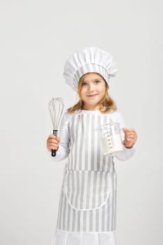 little girl in chef hat and apron with flour in measuring cup and whisk. child dreams of becoming a chef.