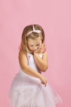 shy little child girl dreams of becoming a ballerina. ballet dancer in pink tutu on pink background
