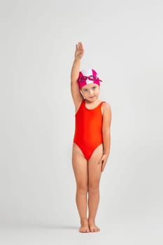 little child girl in swimsuit, swimming goggles and swim cap is preparing for swimmin. Full length. child dreams of becoming a swimming champion