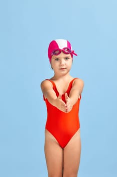 little child girl in swimsuit, swimming goggles and swim cap on blue background. child dreams of becoming a swimming champion