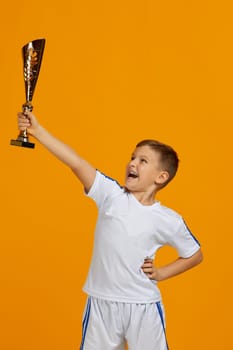 Football player holding a golden cup. little child boy playing soccer and holding trophy on yellow background. kid celebrating success