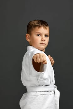 portrait of little child boy in a white karate kimono over gray background. Karate fighter ready to fight.