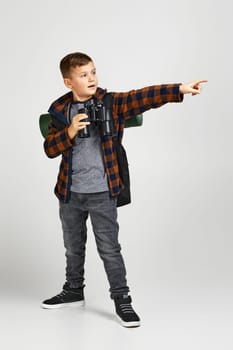 Little boy tourist with backpack holding binoculars pointing to side. Little boy scout dreams of traveling