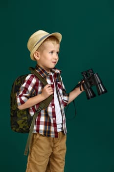 Little boy tourist with backpack holding binoculars. Little boy scout dreams of traveling