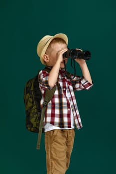 Little boy tourist with backpack looking through a binoculars. Little boy scout dreams of traveling