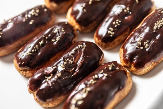 Eight classic eclairs arranged neatly on a white plate. Each pastry features a shiny chocolate glaze and is decorated with delicate golden sprinkles