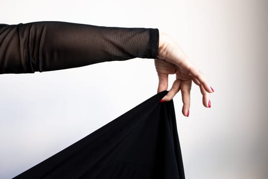 Female hand draping black fabric with red nails and sheer sleeve.