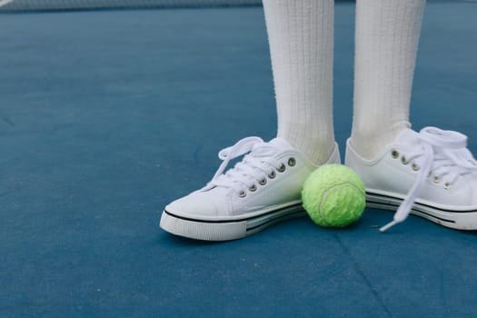 An energetic young athlete showcasing a sporty style on a blue tennis court, with a green tennis ball at their feet, capturing the essence of sports and fitness