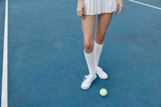 Female athlete dressed in a stylish white tennis outfit poses confidently on a blue court with a tennis ball, capturing the essence of sports and active lifestyle themes