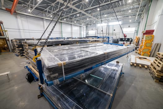 Crane lifting stack of solar panels inside warehouse, industrial production of photovoltaic panels