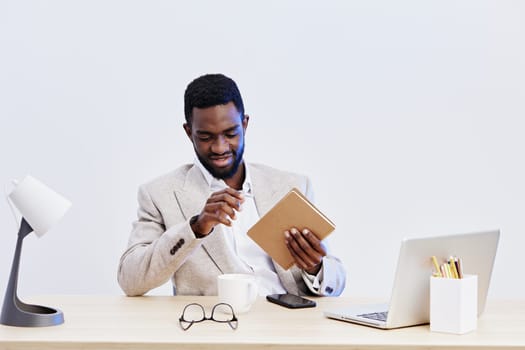 Confident man with cheerful expression using tablet at modern workspace, with laptop, mug, and glasses on desk against plain white background. Photo highlights success, technology use, professional environment, and positive attitude. Concept: workplace productivity.