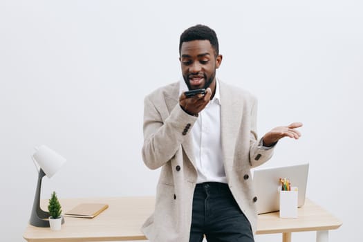 Cheerful man multitasking at a workspace with mobile phone and laptop, smiling, natural lighting, clean minimal office background, friendly and productive mood, suitable for business, communication, technology concepts.