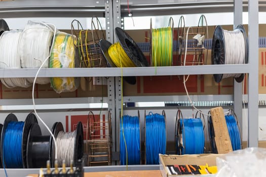 Spools of colorful electrical wires are neatly arranged on metal shelves in a warehouse, ready for use in various electrical projects