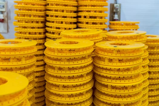 Numerous vibrant yellow plastic cable reels stacked high, creating a striking visual pattern in an industrial warehouse setting, suggesting organized storage or manufacturing processes