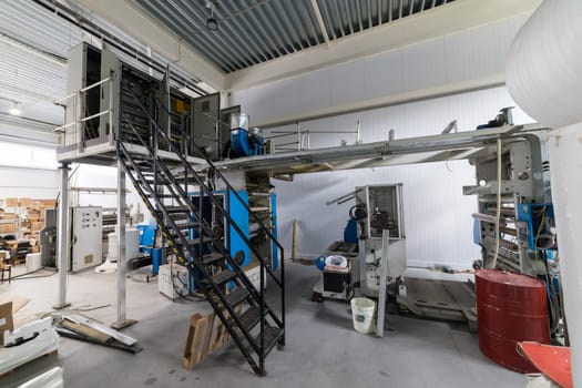 Large industrial printing press standing on a factory floor, surrounded by various equipment and materials, showcasing the scale of modern manufacturing
