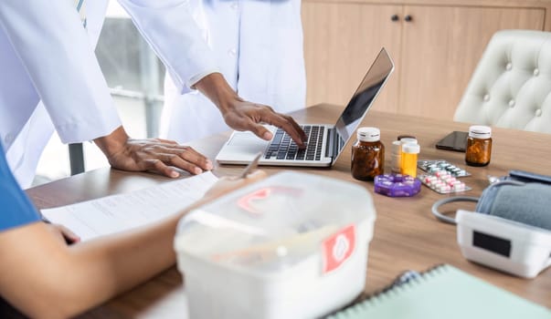 A doctor assisting colleagues with valuable medical data insights displayed on a laptop during a focused meeting.