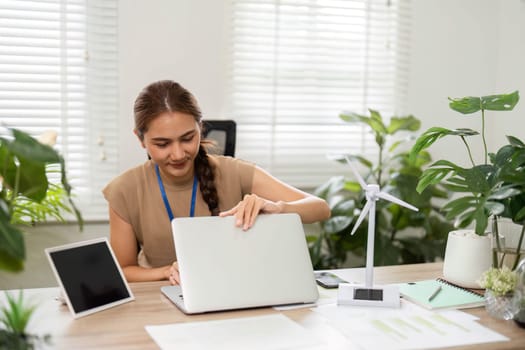 A young woman engaged in productive work on her laptop, surrounded by plants in a bright office, highlighting sustainability and ESG initiatives.