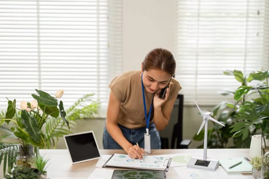 A dedicated young woman organizing sustainability documents while on a phone call, highlighting her commitment to eco-conscious initiatives.