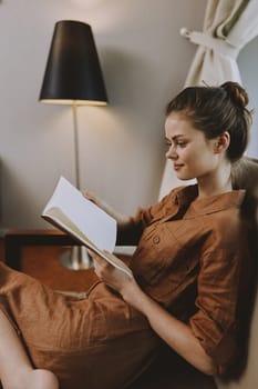 A serene scene of a young woman wearing a brown linen dress, engaged in reading a book in a softly lit room This image portrays tranquility and comfort, ideal for wellness and lifestyle themes