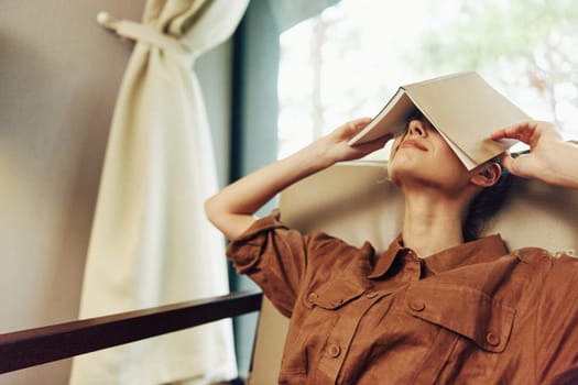 Young woman of Asian descent relaxing in a serene indoor environment, using a book to shield her face from light The warm color palette enhances the cozy atmosphere