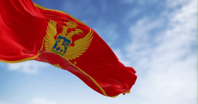 National flag of Montenegro waving in the wind on a clear day. Red with a golden border and features the national coat of arms in its center. 3d illustration render. Selective focus. Fluttering fabric