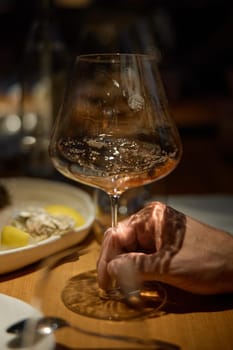 Champagne tasting, Wine glasses are on the table, stylish table setting, A man's hand holds a beautiful elegant glass with rose sparkling wine, an intimate light, a plate with oysters and lemon. High quality photo