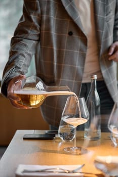 Champagne tasting, The sommelier pours sparkling wine from the decanter into a beautiful glass, Wine glasses are on the table, stylish table setting, sparkling wine bubbles. High quality photo