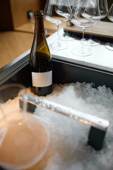 Bottle of champagne is cooled in a niche with ice in the restaurant, local lighting, wine cabinet, decanters for sparkling wine. High quality photo
