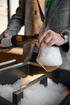 Champagne tasting, The sommelier pours sparkling wine from bottle into the decanter, sparkling wine bubbles, niche with ice. High quality photo