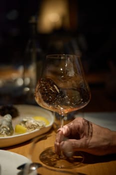 Champagne tasting, Wine glasses are on the table, stylish table setting, A man's hand holds a beautiful elegant glass with rose sparkling wine, an intimate light, a plate with oysters and lemon. High quality photo