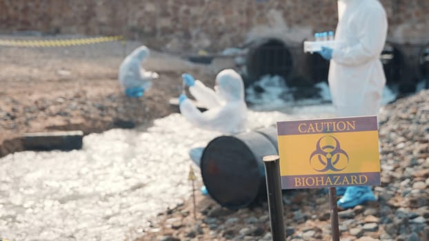 Closeup of chemical warning sign ecologist sampling water from the river in background, Biologist wear protective suit working collects sample of waste water from industrial, problem environment