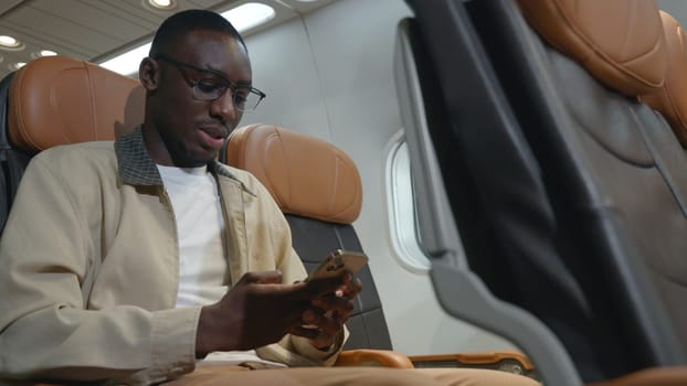 Passenger businessman using mobile phone test wifi connection in plane during flight, Black man typing smartphone read social and news during business trip travelling