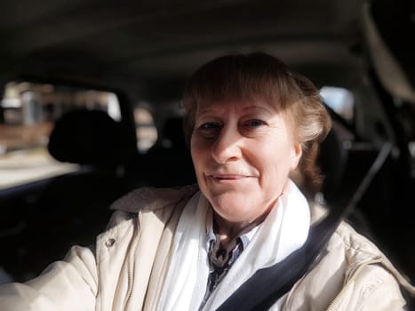 A middle-aged blonde woman takes a cheerful selfie while driving through picturesque scenery on her travel excursion.