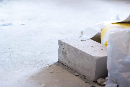 A solid brick is laying on the ground adjacent to a hefty bag of cement, both of which are essential building materials used in construction projects