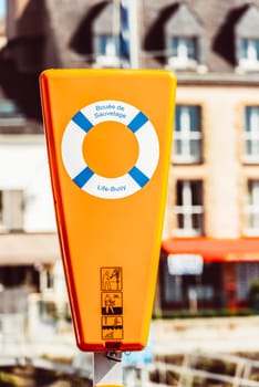 Life buoy in bright orange container by quaint buildings, safety concept, 