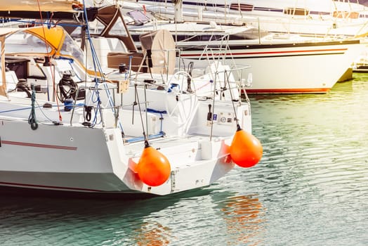 Yacht with orange buoys docked at marina, calm sea reflecting light, 