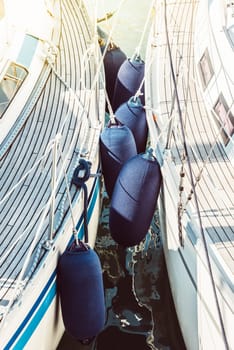 Sailboats with protective fenders anchored at marina, sunlight creating reflections, 