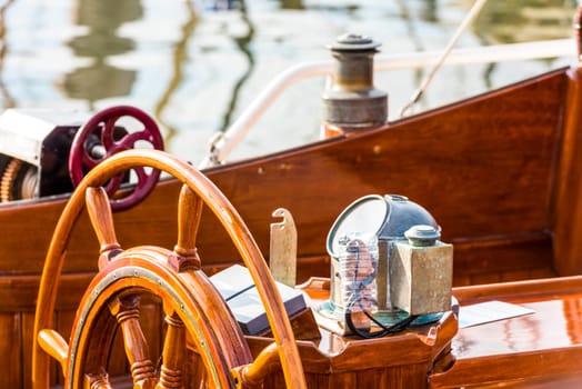 Sailboat helm with wooden wheel and nautical equipment in sunlight, background, 