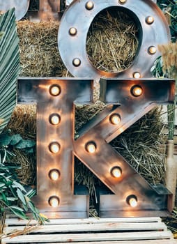 Illuminated metal letter K against a rustic hay background, 
