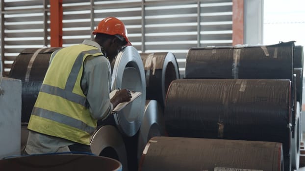 Two black workers engineer factory textile inspection and checking inventory levels of goods of roll metal sheet roof in warehouse they talking together and do work with products ready for shipment