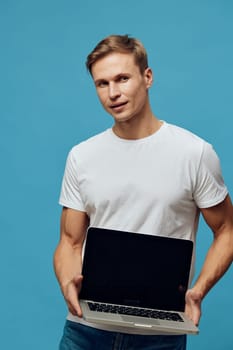 young man holding laptop with blank screen look camera casual wear white t-shirt blue background representing remote work digital nomad freelance online jobs technology concept