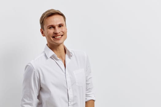 Smiling man in white shirt holds phone and looks confident standing isolated on light background representing AI chat technology digital communication and remote connectivity concept