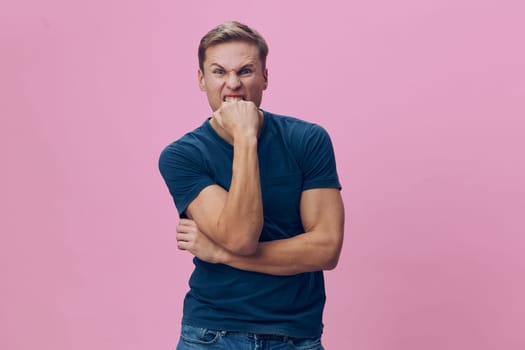 Portrait of cheerful man with confident expression, wearing casual blue t-shirt and jeans, standing with arms crossed and hand on chin in front of pink background. Close-up shot capturing joyful, relaxed mood, modern style, lifestyle concept, positive attitude, studio setting.