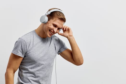 Happy man in gray casual t-shirt listening to music with wireless headphones, smiling and relaxed, isolated on a white background. Concept: joy of music and leisure
