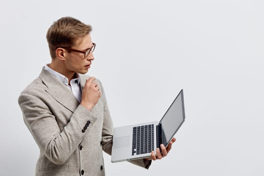 serious caucasian man holding laptop looking at screen wearing striped beige blazer and glasses isolated on gray background focused on digital nomad lifestyle and remote work concept