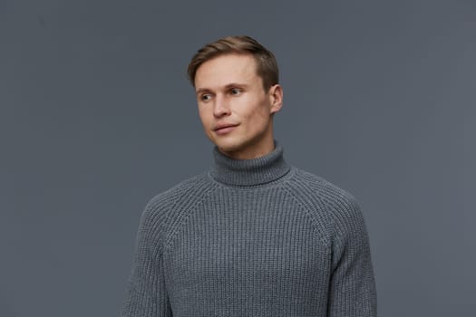 young man thoughtful wearing gray turtleneck sweater looking sideways on plain gray background studio portrait casual fashion clothing mental health and gadgets concept emphasizing modern lifestyle and wellness