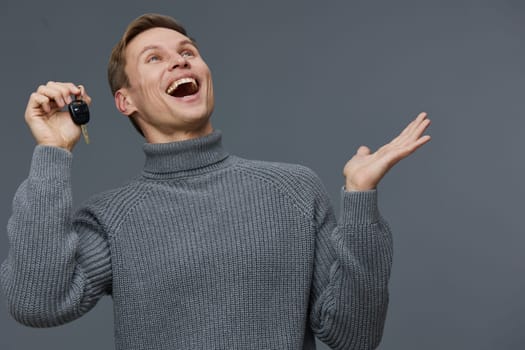 excited man holding car keys in hand wearing knitted gray sweater smile looking up isolated on solid gray background digital nomad freelance technology concept freedom and success