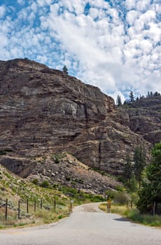 Gated gravel road leading to the mounain area in Canada with bluesky and mountain texture background. Vertical panorama