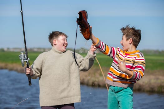 Funny fishing. Two of the boy's friends hooked an old shoe with a fishing rod and are laughing.