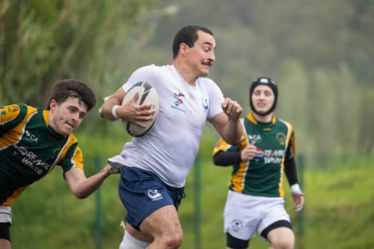 3 may 2025, lisbon. Portugal - oeiras vs ag - rugby player running with the ball, chased by opponents, during a rainy match
